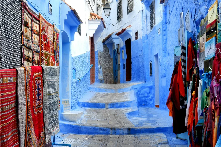 Handwoven rugs and clothes for sale in a blue street of Chefchaouen, day 4 of the 14-Day Morocco Tour from Casablanca: Morocco at Leisure
