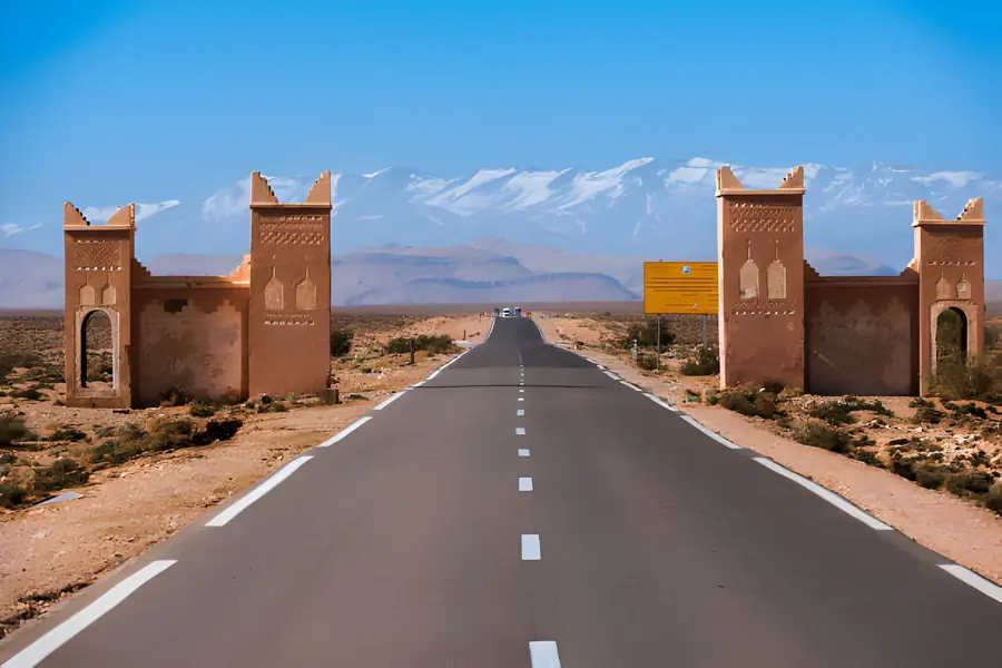 Road between Agdz and Ouarzazate with kasbah-style gates and the snowy High Atlas, day 3 of the 4-Day Marrakech to Merzouga Desert Tour