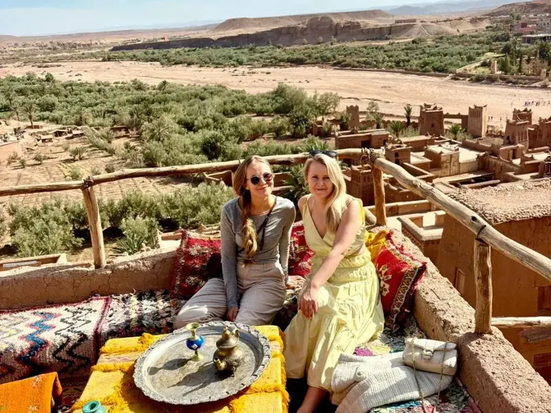 Two travelers having mint tea on a rooftop terrace overlooking the Ait Ben Haddou kasbah