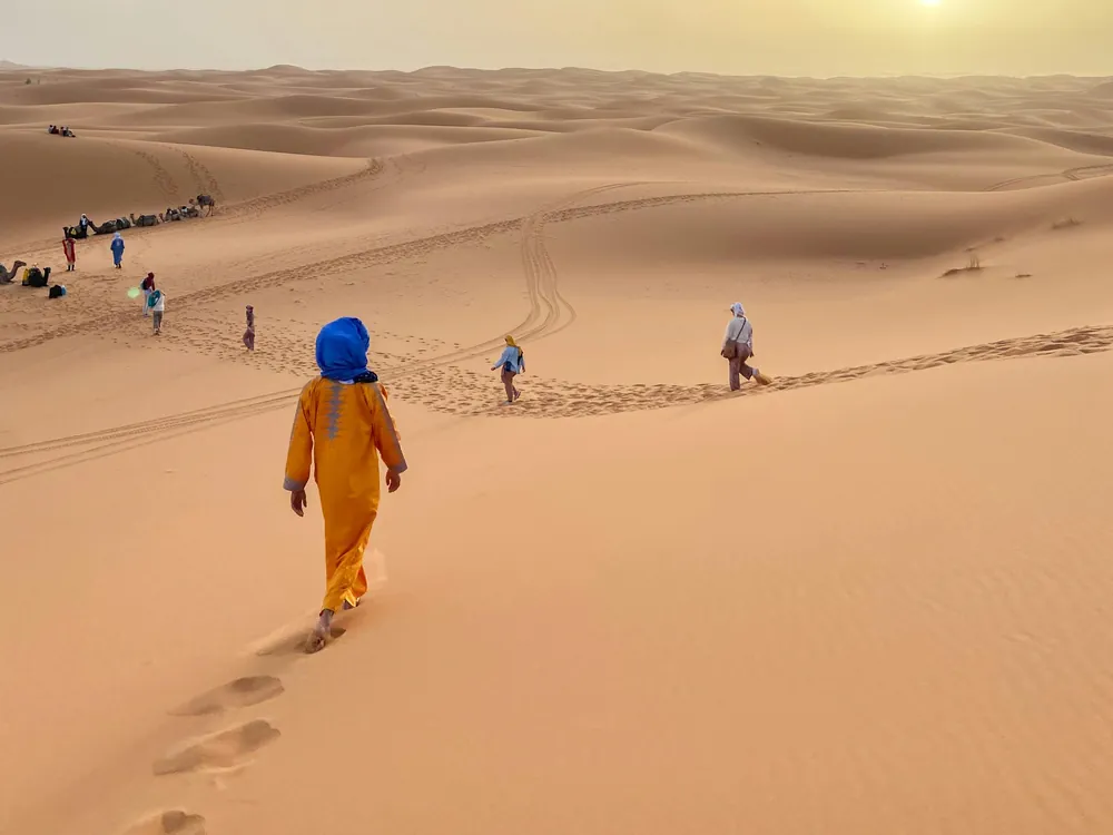 Travelers walking down the Erg Chebbi dunes to their camels at sunset on a 3-day desert tour from Fes to Merzouga
