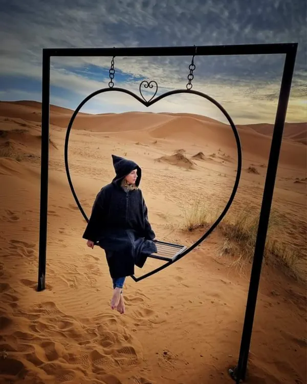 Guest on a heart-shaped swing facing the Sahara dunes near the Merzouga camp