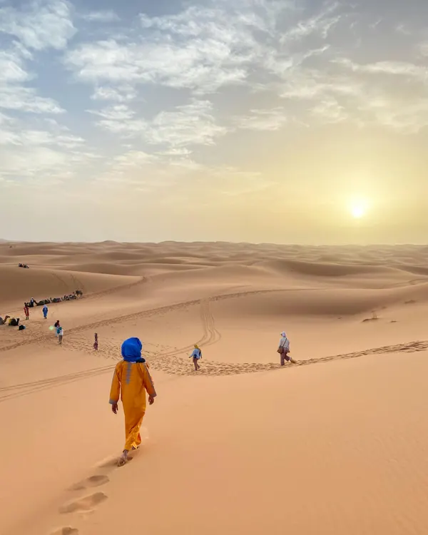 Traveler in a Moroccan djellaba walking on the Erg Chebbi dunes at sunset, Merzouga